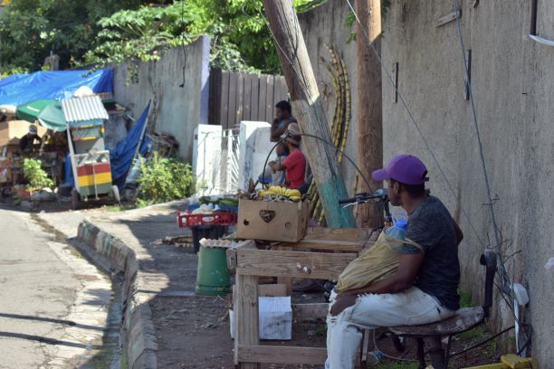 A Jamaican street with a few vendors sand a leaning telephone pole