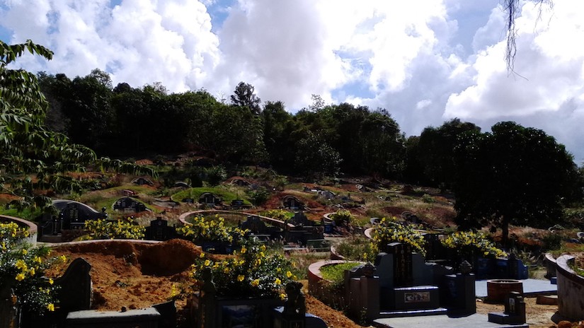A landscape scene of cemetary on a small hill with a dozen or more headstones beneath a cloudy blue sky.