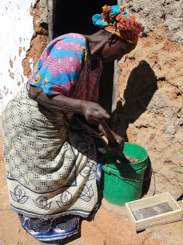 Woman, holding a wooden stick, stirs a mixture in a plastic bucket
