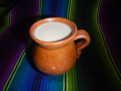 An orange mug holds a milky white liquid and sits on a blue and green striped woven blanket.