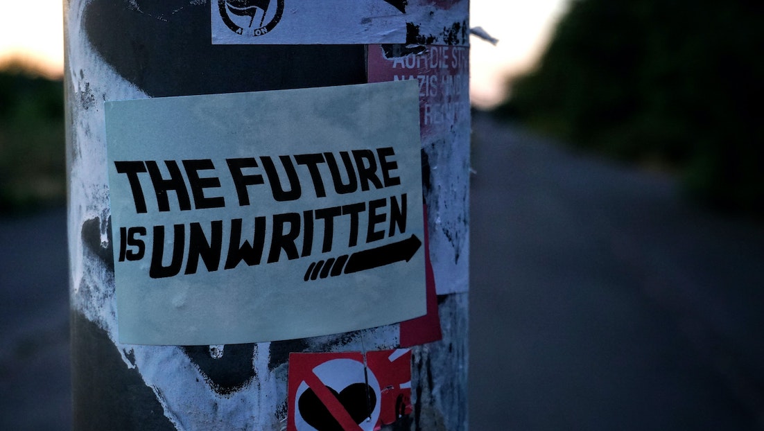 Outside adrtising pillar with a sign wrapped around it which reads 'The Future Is Unwritten' 