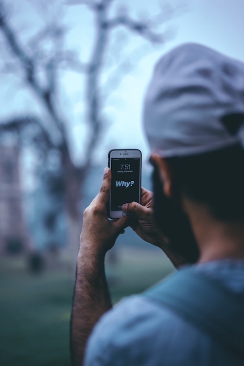Person looking at their smart phone crisp image with background of tree blurry.