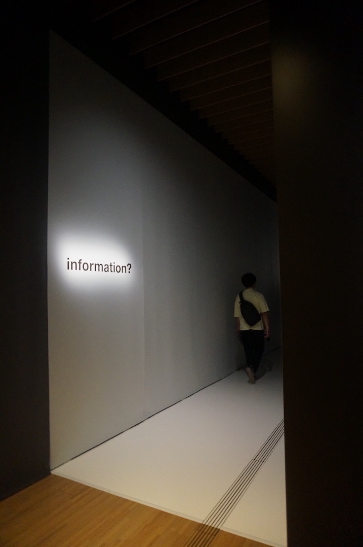 A corridor at the beginning of the exhibition in the Suntory Museum of Art. It is dimly lit, with the word "information?" lit up on the wall.