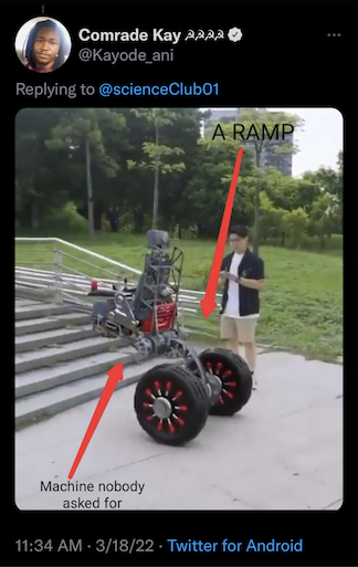 A complex metal frame sits precariously over two large hydraulic wheels. This is a stair climbing wheelchair. It faces a set of stairs. A person stands behind it with controls. The image has an arrow pointing toward the chair that reads "machine nobody asked for". Another arrow points behind the person and behind the stairs where a ramp can barely be seen. It is labled "A RAMP."