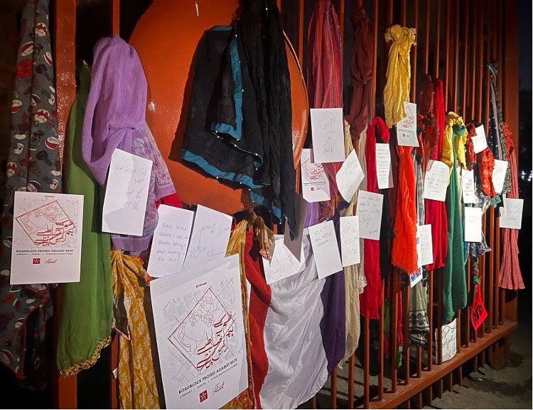 Pieces of paper and dupattas of many colors hanging on a red metal gate.