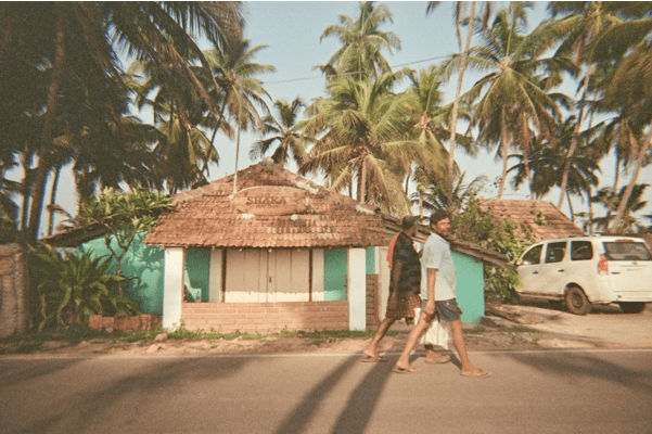 Two men walking along the street in front of the Shaka house decorated with palm trees and sunshine
