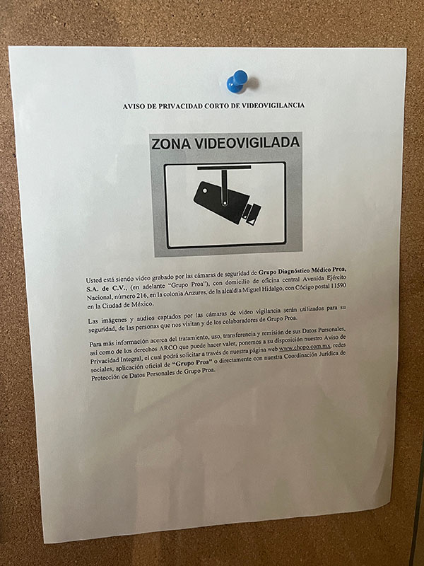 A cork bulletin board has different documents pinned to it, including one in Spanish titled, “Short privacy notice for videosurveillance.” It includes a symbol featuring a camera and a banner that says “videosurveilled area” and boilerplate text.