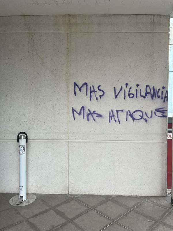 The wall of a public university building has purple graffiti that reads in Spanish, “more surveillance, more attacks.” 