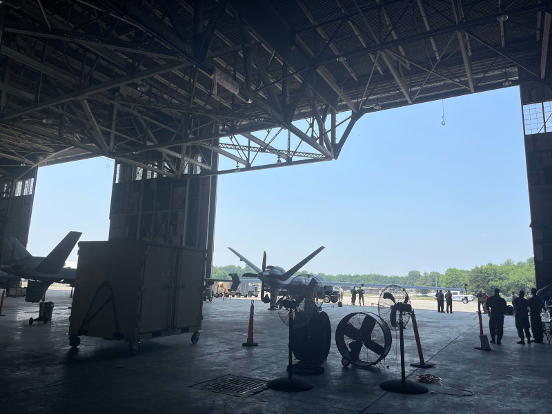 Two aircrafts are parked in a hangar with personnel standing nearby.