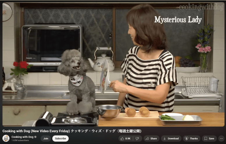 A screenshot of the YouTube cooking show "Cooking with dog" focuses on a grey poodle and woman in the kitchen. They are centred and looking at eachother, the poodle Francis is smiling and the human host has her head turned away from the camera and towards Francis. The backdrop is a kitchen.