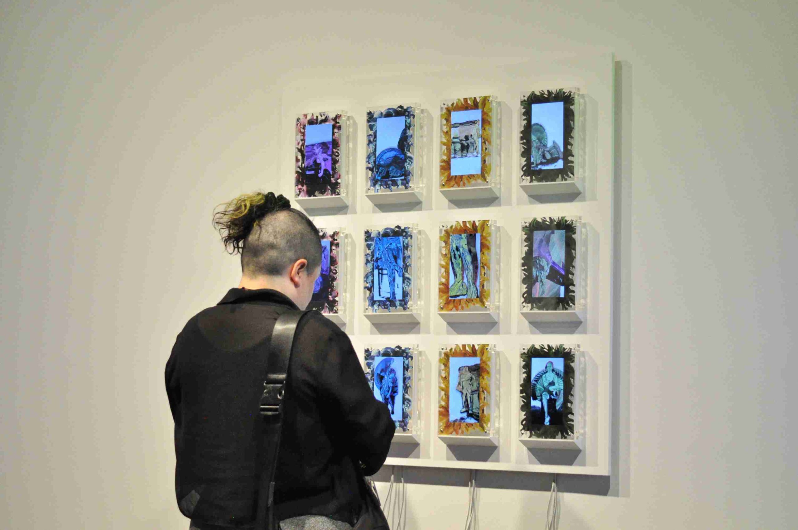 A candid photo showing the Disabled Body In Motion installed at Centre Clark. The 12 acrylic frames are anchored to the wall in a colorful grid pattern. A viewer is watching the animations unfold. 