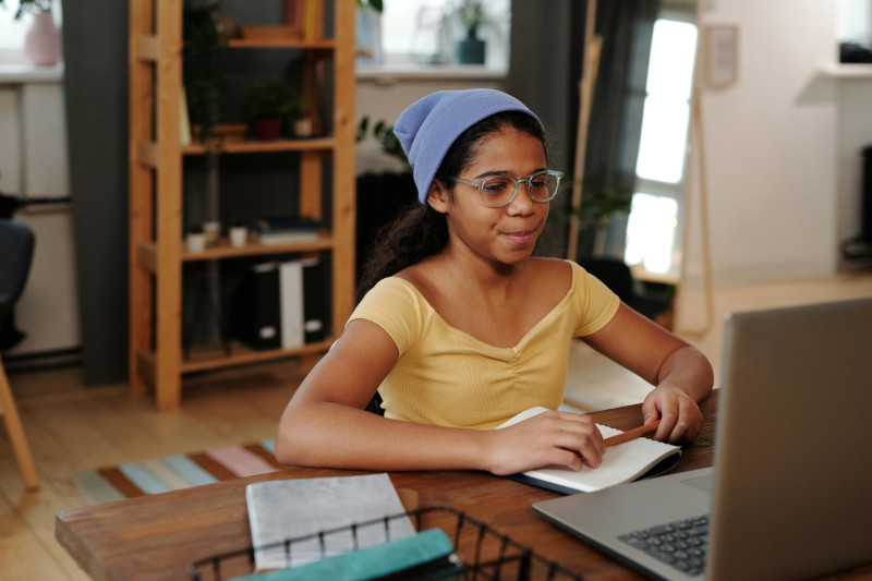 child sitting at a computer with a note book 