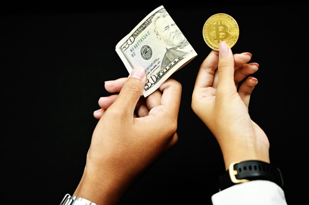 Picture of two hands, one holding a 50 American dollar bill and another holding a bitcoin gold.