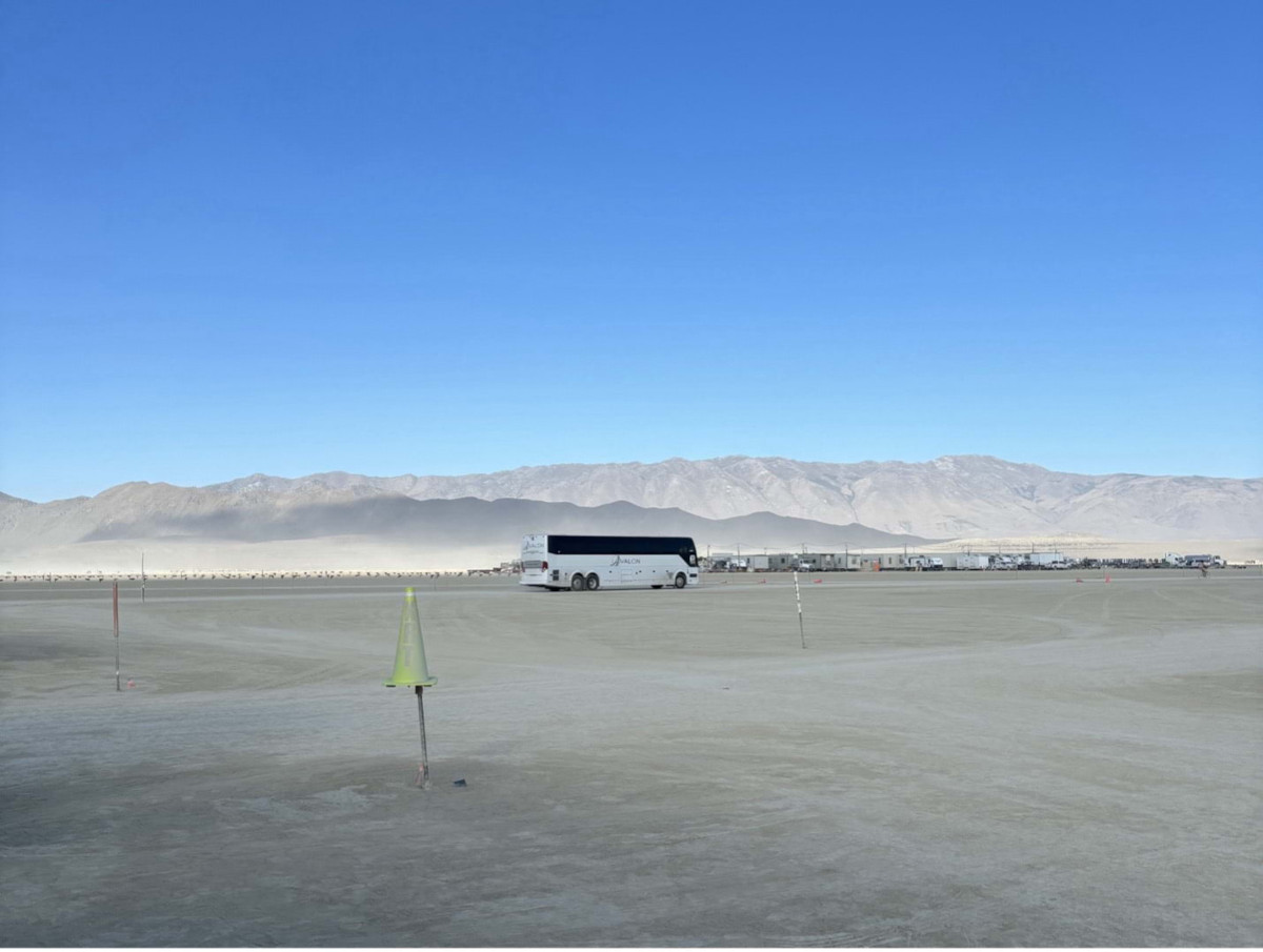 A bus drives into a dusty landscape with a blue sky