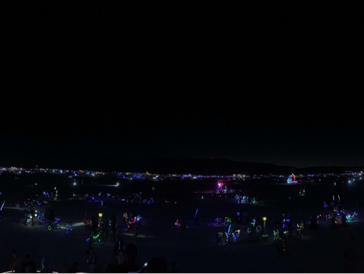 A landscape in the dark, with colorful lights in the distance.
