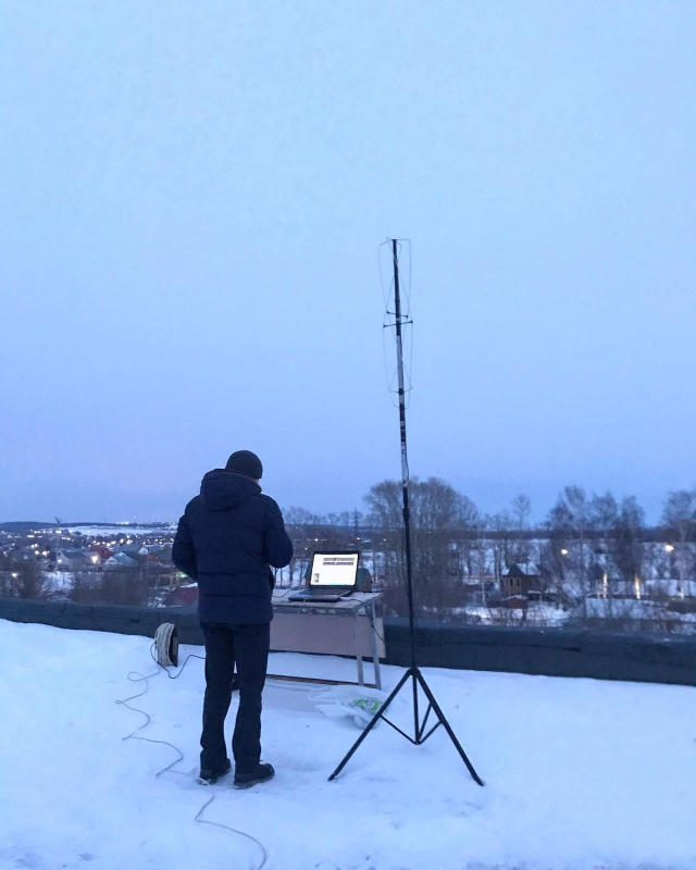 Man wearing jacket stands outside in the snow looking at a monitor.