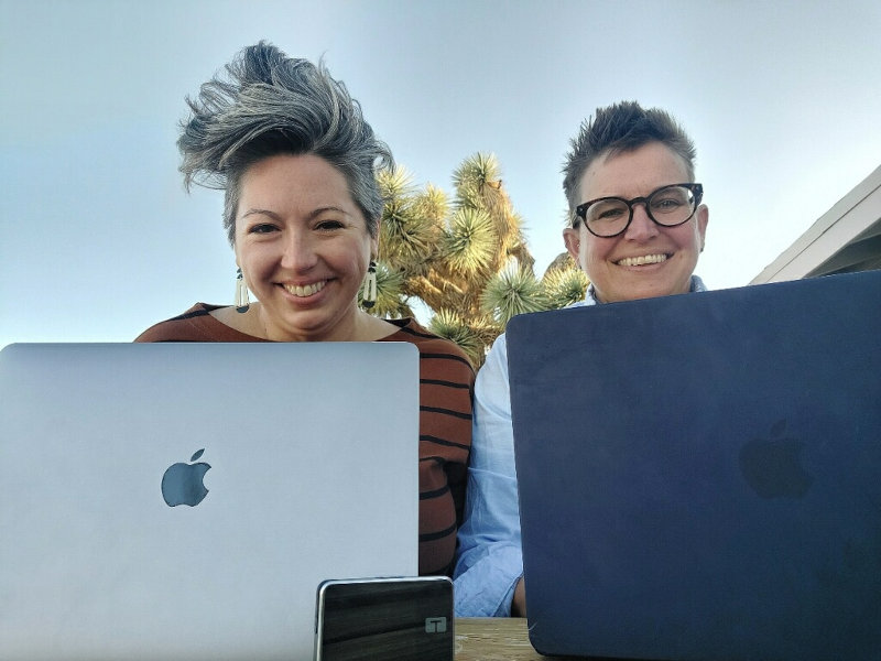 Two people smiling and seated at laptops.