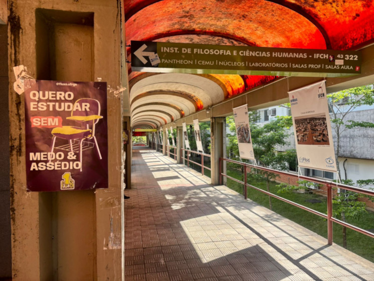 The image shows a university environment, with a poster prominently displayed that reads "I want to study without fear and harassment."