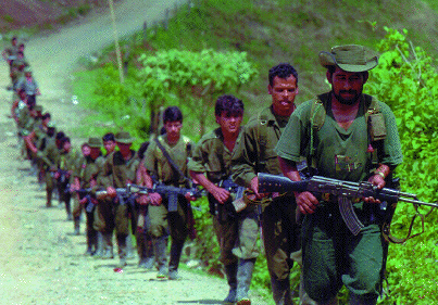Group of armed guerrilla fighters standing in a rural outdoor setting, holding rifles and wearing military-style clothing.