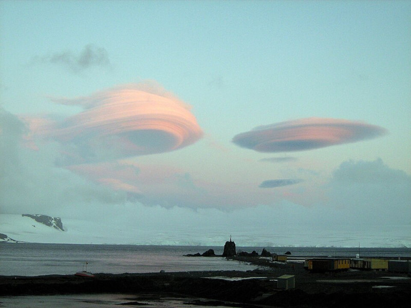 Two lenticular clouds, looking a bit like classic images of UFOs, hovering over a landscape with snow and rocks.