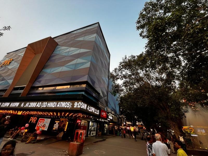 The PVR Anupam multiplex building. People in groups of 2-5 members are standing around the building and chatting. 