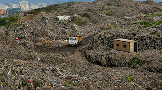 A white waste truck moves across the slopes of waste in a dumping ground.