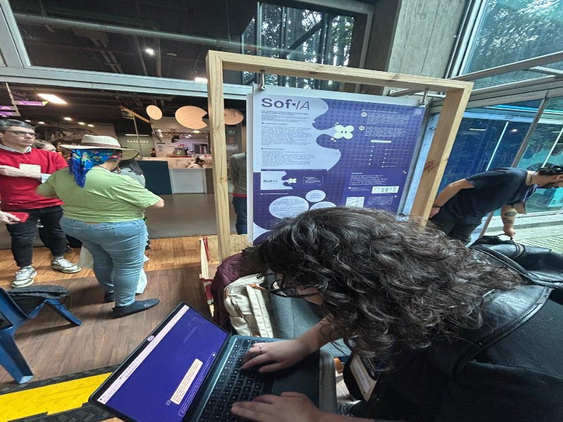 A person with a computer in the foreground, with university conference posters and several people in the background.