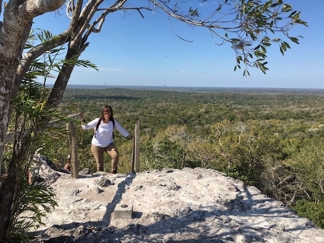 Woman standing on the top of a ruin overlooking the vast, green canopy of the Maya Biosphere Reserve