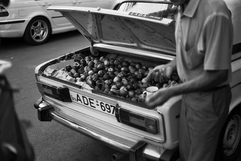 A man is selling fruit out of the booth of his car