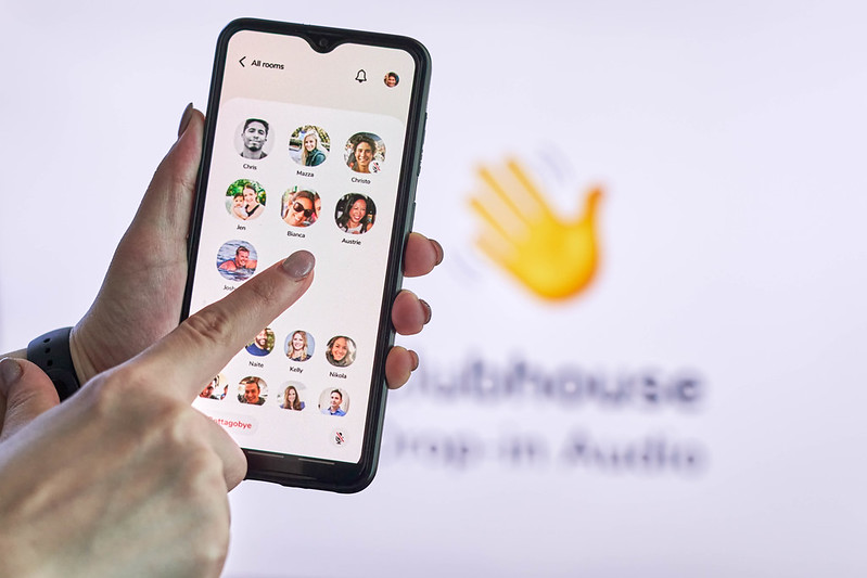 A hand flipping through the phone Clubhouse app; in front of a Clubhouse app