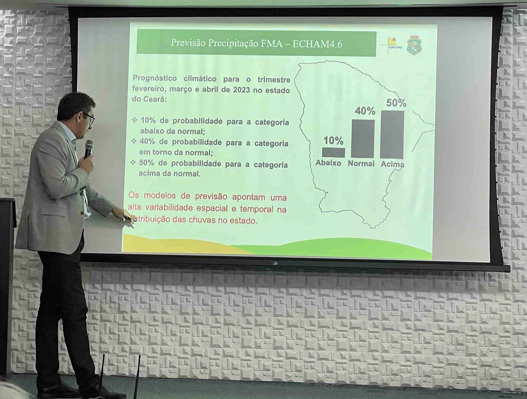 Dr. Eduardo Sávio Martins of Funceme pointing to presentation slide with seasonal forecast information indicating probabilities of rainfall of 10 percent below average, 40 percent around average, and 50 percent above average. Text in red states that the models indicate high spatial and temporal variability for rainfall.
