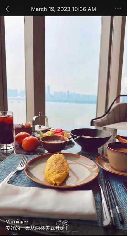 A window-side table with an omelette, fruit, and coffee served on top. The water and city skyline are visible in the window.