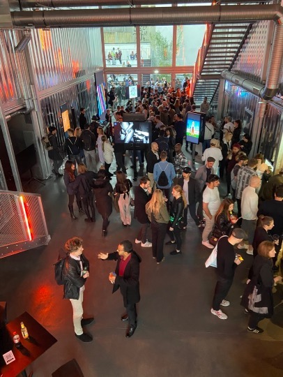 A crowded event at an art gallery. Artworks are displayed on television screens.