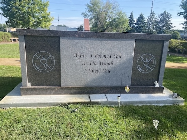 A granite memorial stone standing in a cemetary. The memorial stone reads: "Before I formed you / In the womb / I knew you"