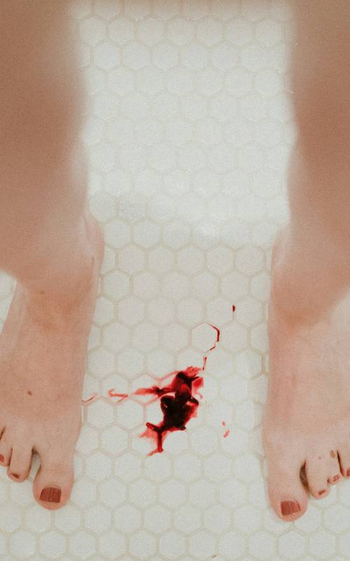 Feet of a woman and a bloodstain in the floor.